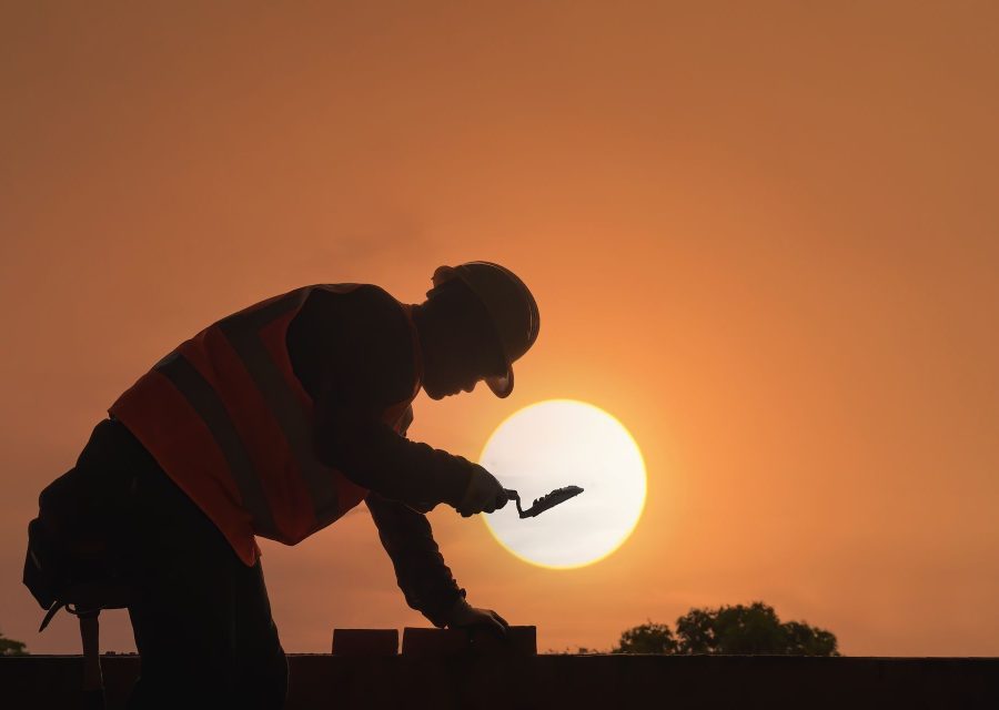 Maurer arbeitet mit der Kelle an einer Mauer im Abendlicht